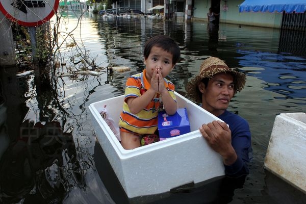 泰國水患發生至11月24日已超過4週，曼谷市中心幾乎逃過水患危機，但北邊的巴太省蘭實區水患還未消退，社區居民聽到救援隊抵達，許多人划船、涉水領取物資。這位父親把兒子放在保麗龍箱子內，外出領取物資。