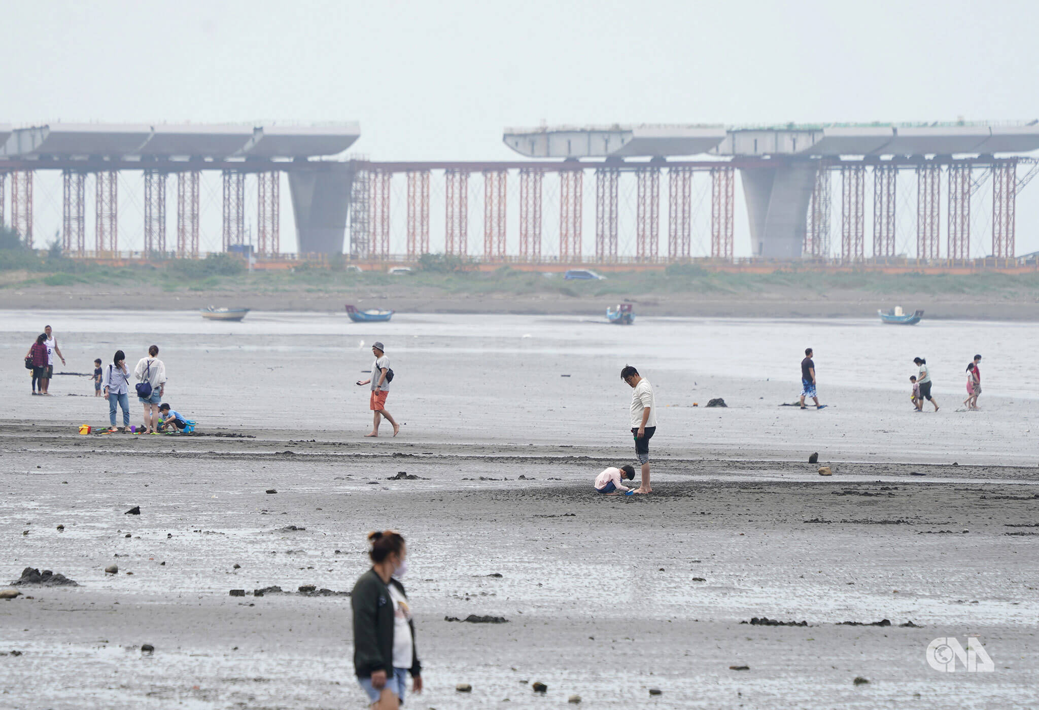 退潮時民眾八里左岸遊憩，遠方興建中的淡江大橋。